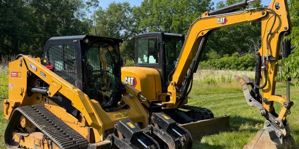 Two yellow Caterpillar construction machines parked on grass.