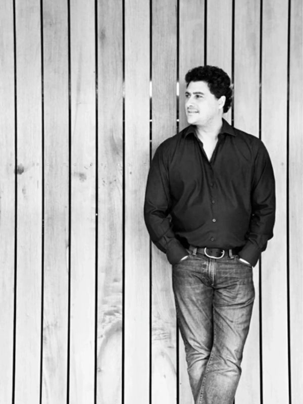 Man in black shirt and jeans leaning against wooden wall.