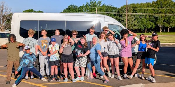 Group of teens posing playfully in front of a white van on a sunny day.