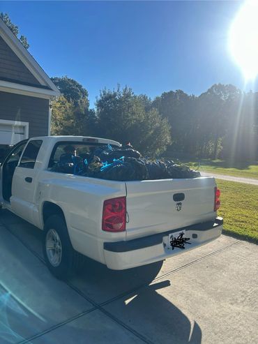 White pickup truck filled with black garbage bags in bright daylight.