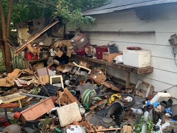 A cluttered yard filled with various discarded items and debris beside a building.
