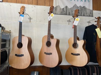 Three acoustic guitars hanging on a wall in a store.
