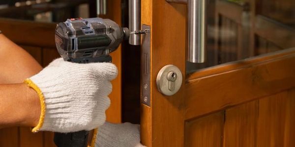 Person using a power drill to install a door handle on a wooden door.