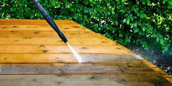 Pressure washing a wooden deck to clean dirt and grime.