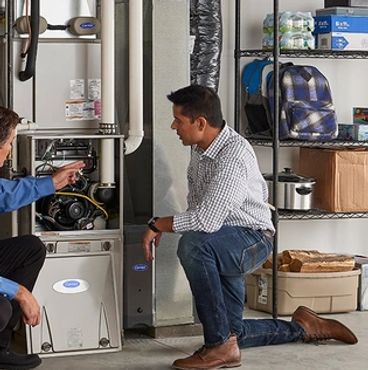 Two men inspecting a furnace in a garage or utility room.