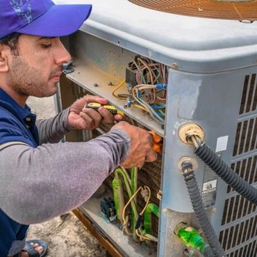 Technician repairing an outdoor air conditioning unit with tools.