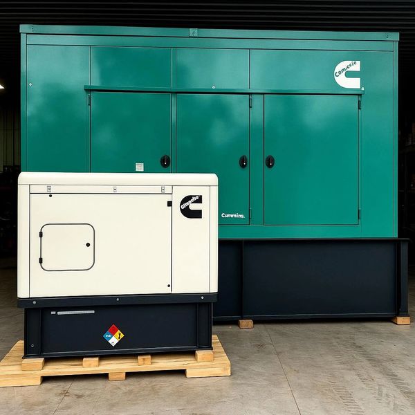 Two industrial generators, one white and one green, placed on wooden pallets indoors.