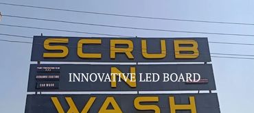 Signboard of Scrub N Wash car cleaning service against a clear sky.