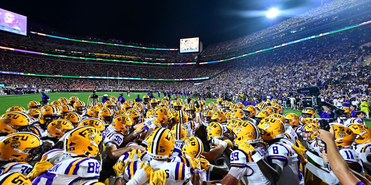 LSU Tigers football team huddles on the field at night.
