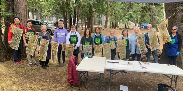 Group of people displaying leaf prints on fabric outdoors.