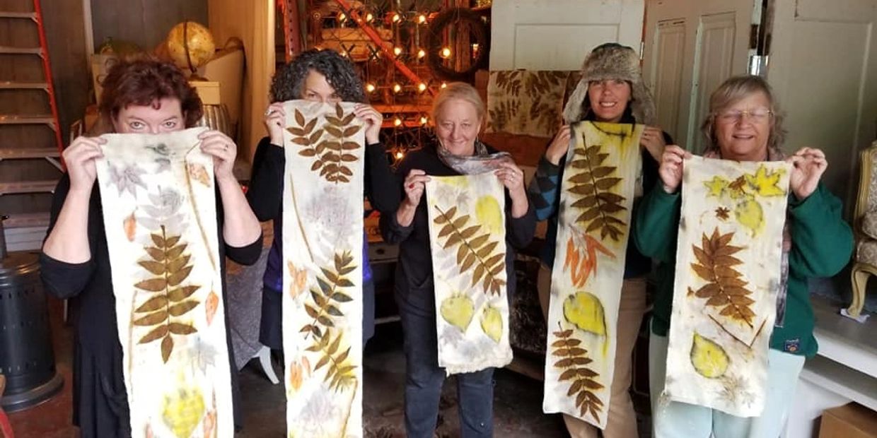 Five people holding long fabric strips with pressed leaves.