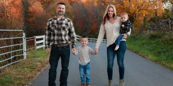 Family of four holding hands on a country road with autumn trees in the background.