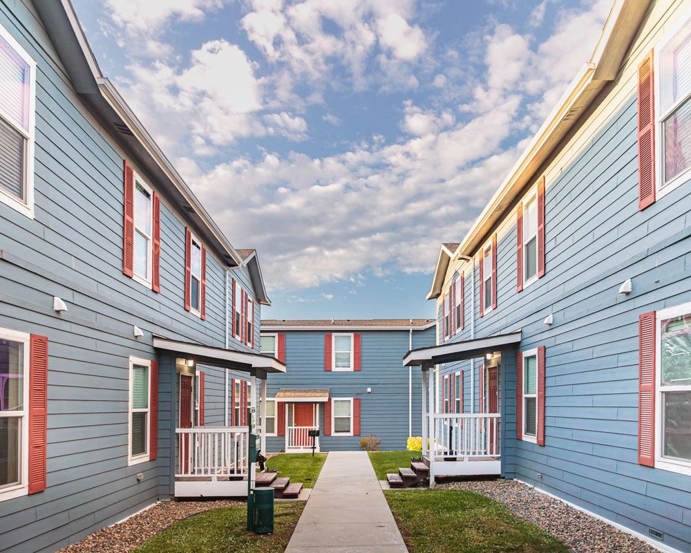 Image of a charming exterior with blue siding and burgundy shutters, grass, and sidewalk