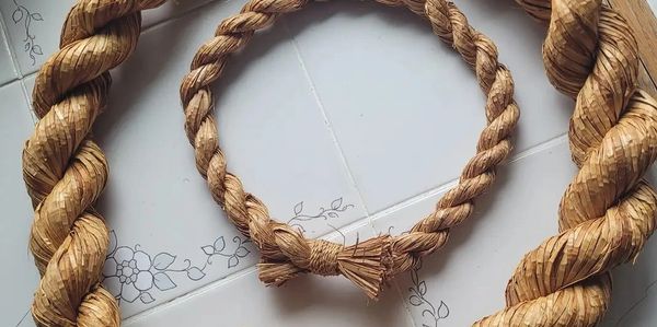Handwoven straw rope coiled on tiled floor with floral patterns.