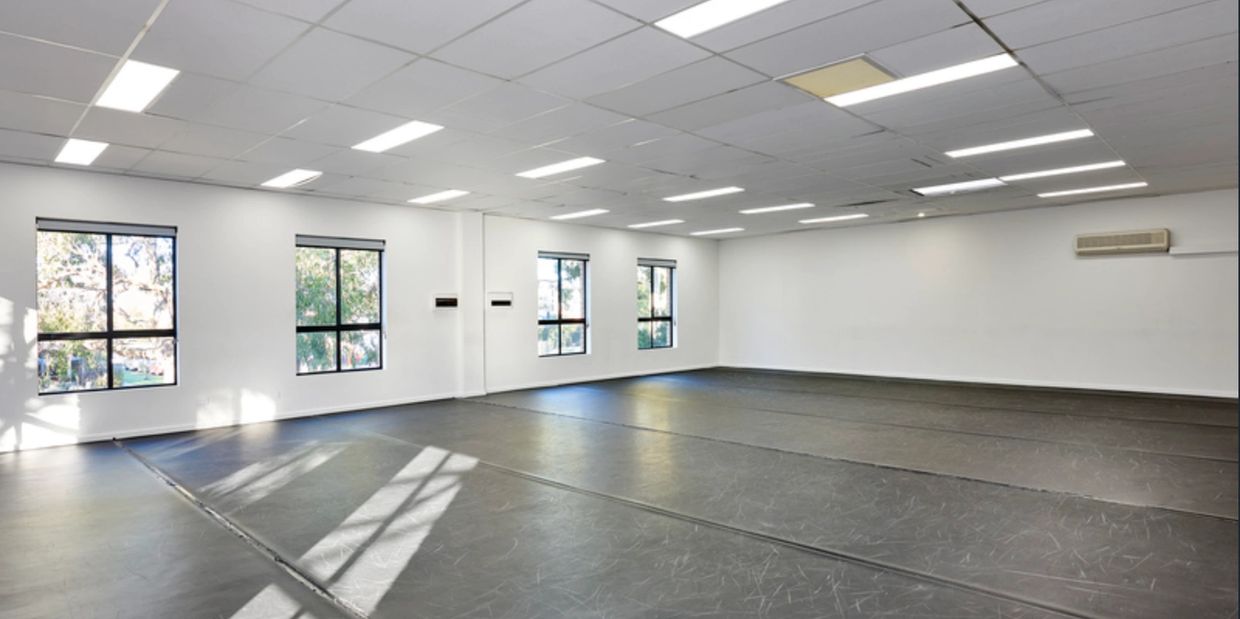 Spacious empty dance studio with large windows and overhead lights.