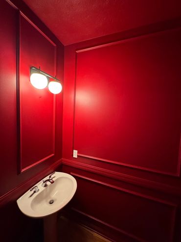Small bathroom with bold red walls and a white pedestal sink under bright wall lights.