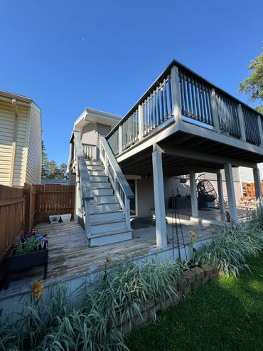 A two-level wooden deck with stairs leading to the upper level under a clear blue sky.