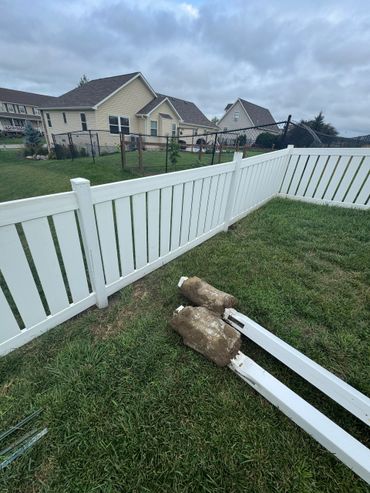 Broken white fence panels lying on the grass in a suburban backyard.