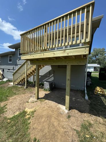 Newly constructed wooden deck with stairs attached to a house on a sunny day.