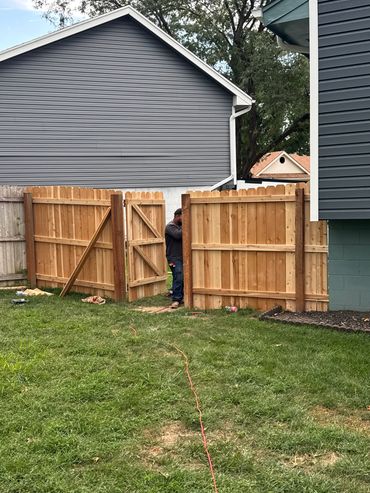 Man working on a new wooden fence gate in a backyard.
