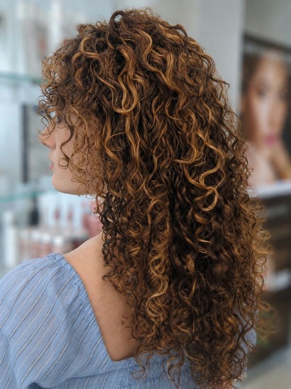 Side profile of a woman with long, curly, highlighted hair.