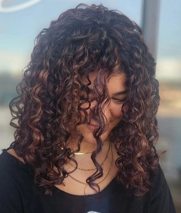Woman with glossy, curly hair smiling shyly.