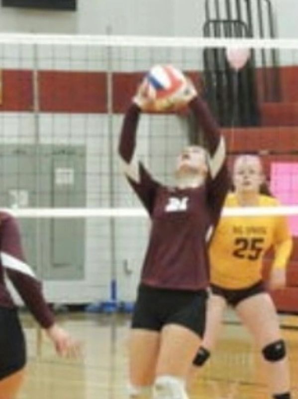 Volleyball player in maroon jersey sets the ball during a game.