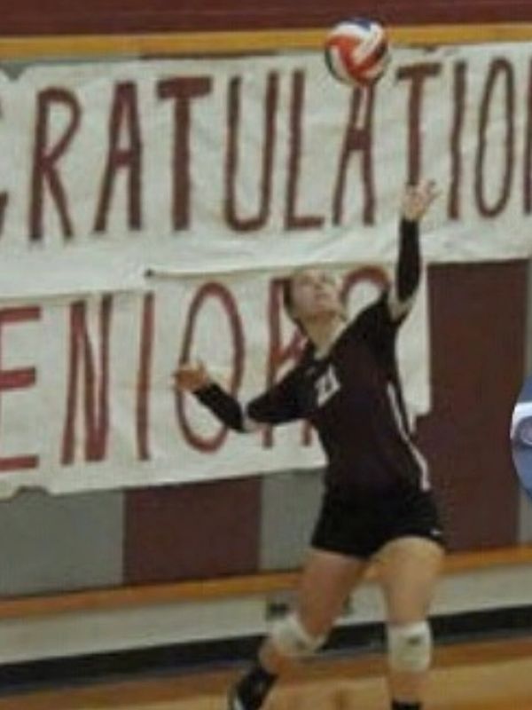 Volleyball player hitting the ball in front of a senior congratulatory banner.