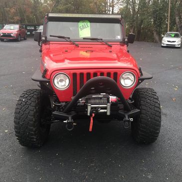 Front view of a red Jeep with off-road tires and a winch, parked for sale.