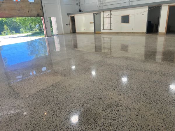 Polished concrete floor reflecting lights and outdoor greenery in an empty garage.