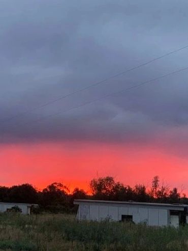Sunset casting vibrant red and purple hues over rural buildings and trees.
