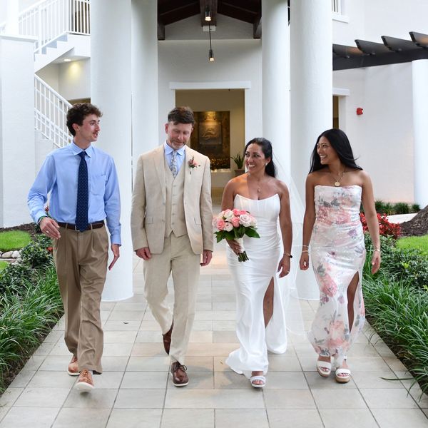 Two couples walking together outdoors, dressed formally.