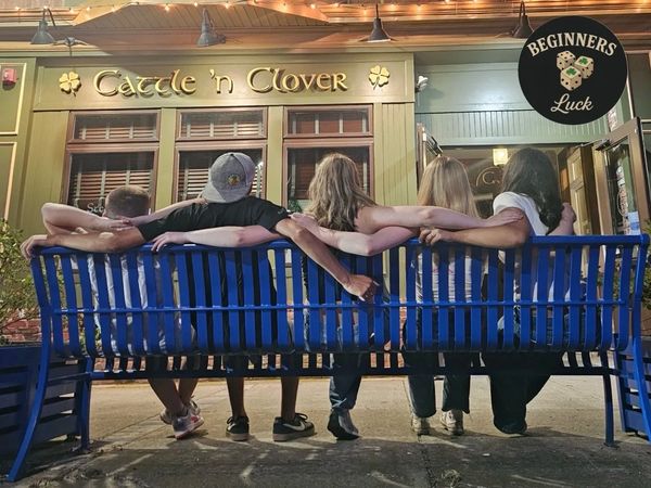 Friends linked arm in arm on a blue bench outside Cattle 'n Clover.