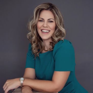 Smiling woman with blonde curly hair in teal dress.Prosper Media Services