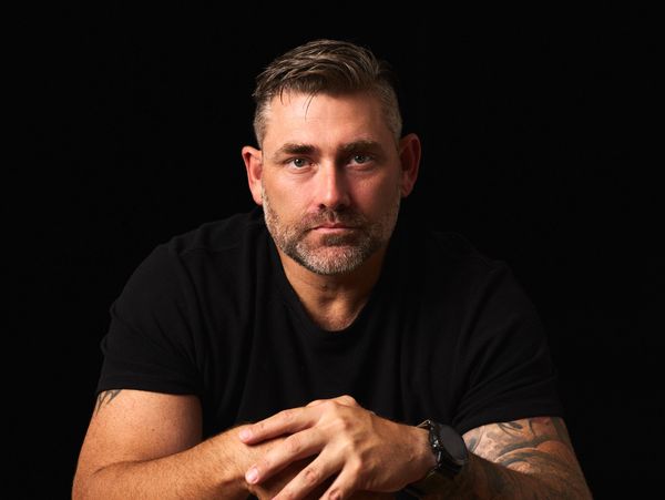 Serious man with tattoos and a black t-shirt against a black background.