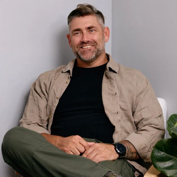 Smiling man sitting comfortably with casual attire and a watch.