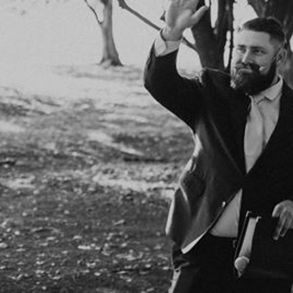 Man in suit waving outdoors with a joyful expression.
