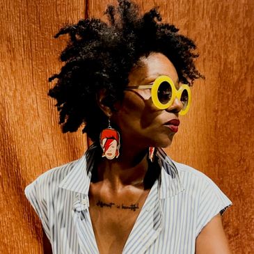 Woman with afro hairstyle wearing yellow sunglasses and artistic earrings.