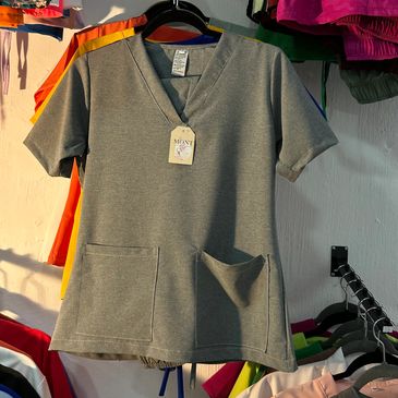 Camiseta gris con cuello en V y dos bolsillos delanteros.