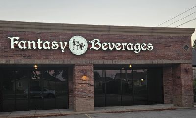Storefront of Fantasy Beverages with a brick facade and illuminated sign.