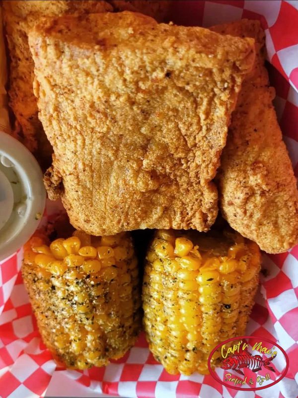 Several hand-breaded, seasoned & fried filets of Mahi Mahi paired w/ peppered corn cob halves