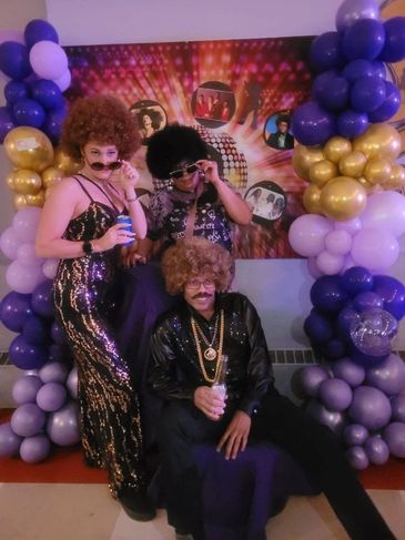 Three people in disco-themed costumes posing with wigs and fake mustaches.