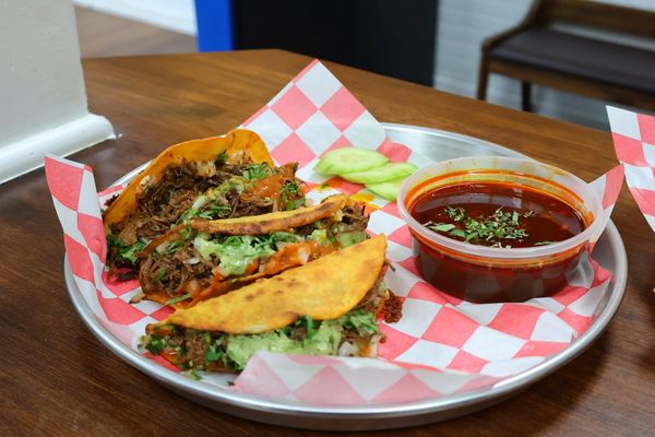 Plate of tacos with dipping sauce and cucumber slices.