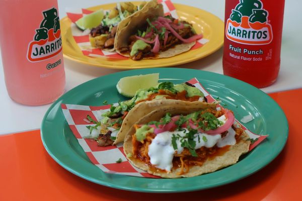 Two plates of tacos with Jarritos sodas.