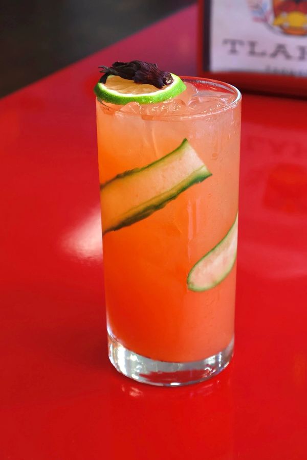 Orange cocktail with cucumber garnish on red table.