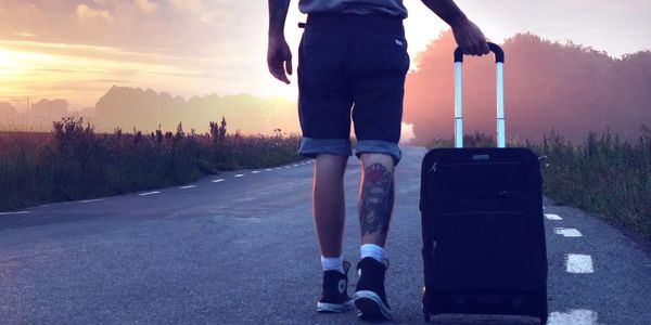 Person walking on a road with a suitcase during sunset.