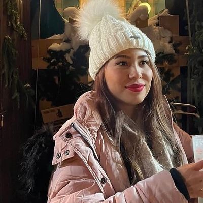 Young woman in a white knit hat and pink jacket smiling indoors.