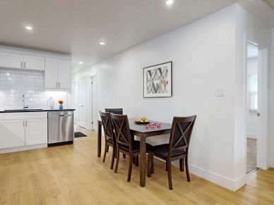 Modern kitchen and dining area with wooden floor and white cabinets.
