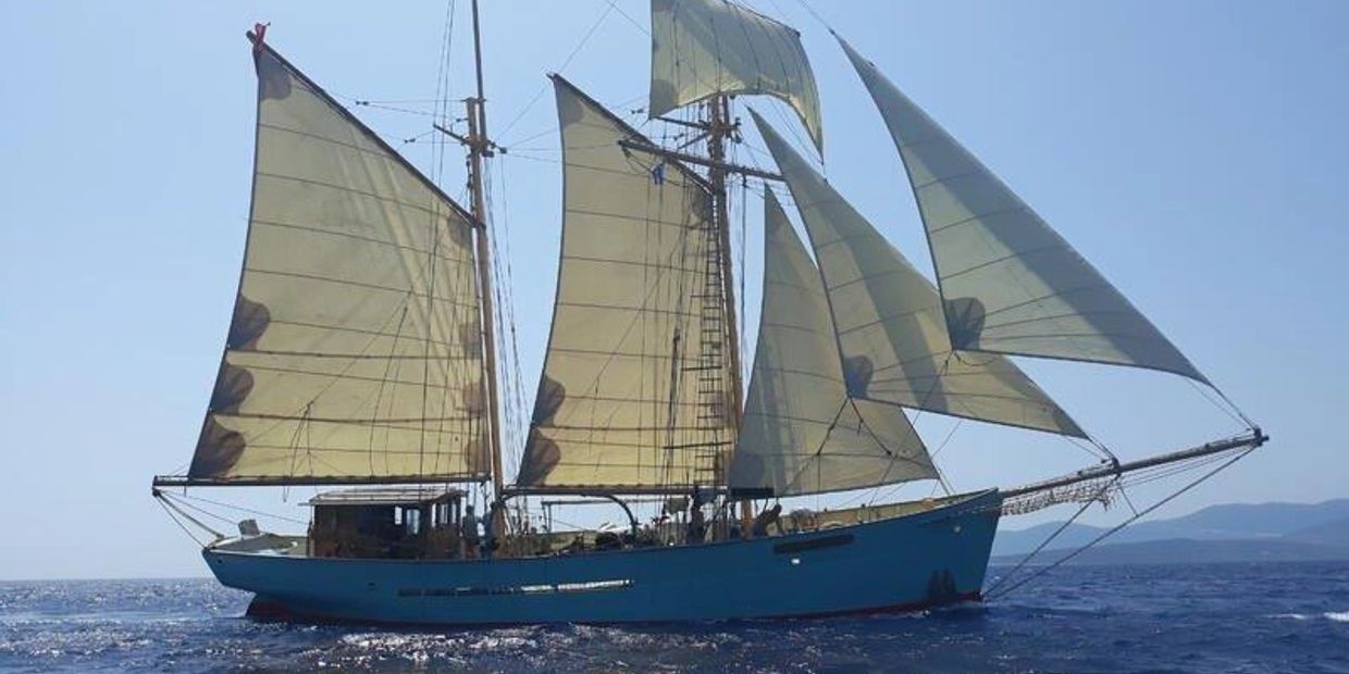 A blue sailing ship with multiple beige sails on the sea.