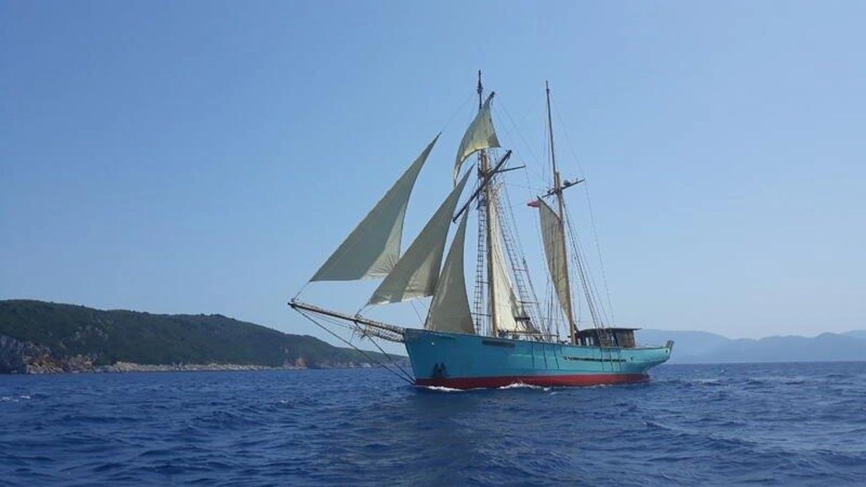 Sailboat with blue hull sails on calm sea.